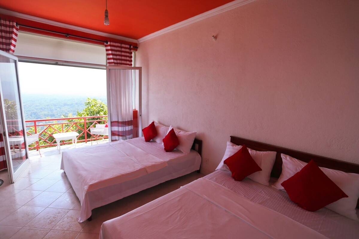 Habitación de hotel con dos camas, un balcón con baranda roja y vistas al paisaje.
