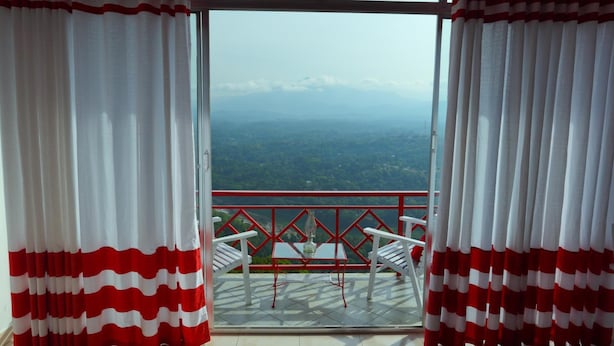 A balcony with a table and chairs, a view of a mountainous landscape, and red and white curtains. - Redhill Kandy (Kandy)