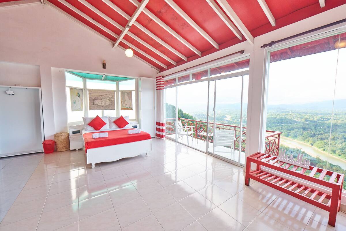 Un dormitorio amplio con una cama grande, un balcón con vistas y un banco rojo.
