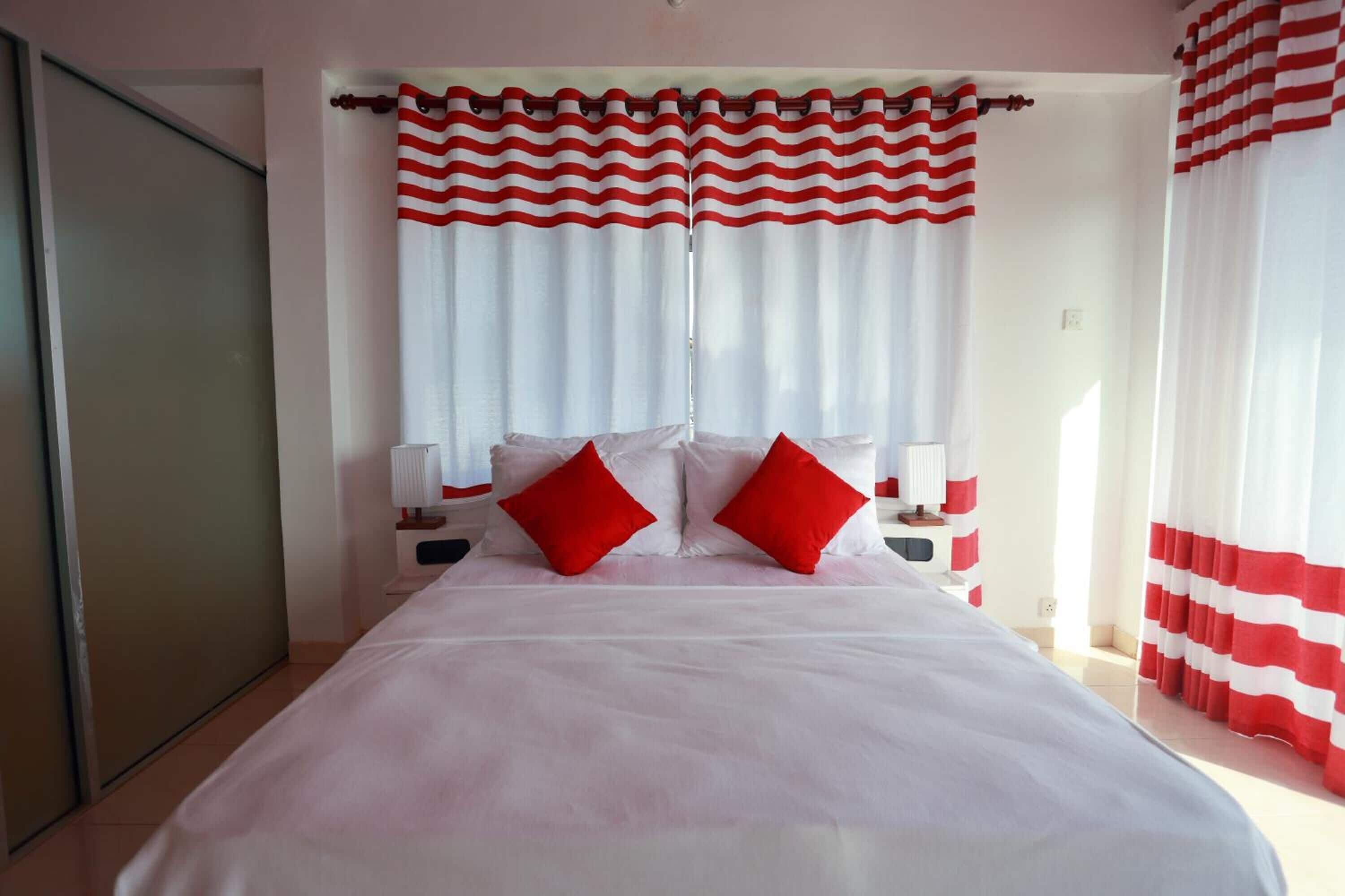 A hotel room with a large bed, red and white curtains, and two bedside tables with lamps.