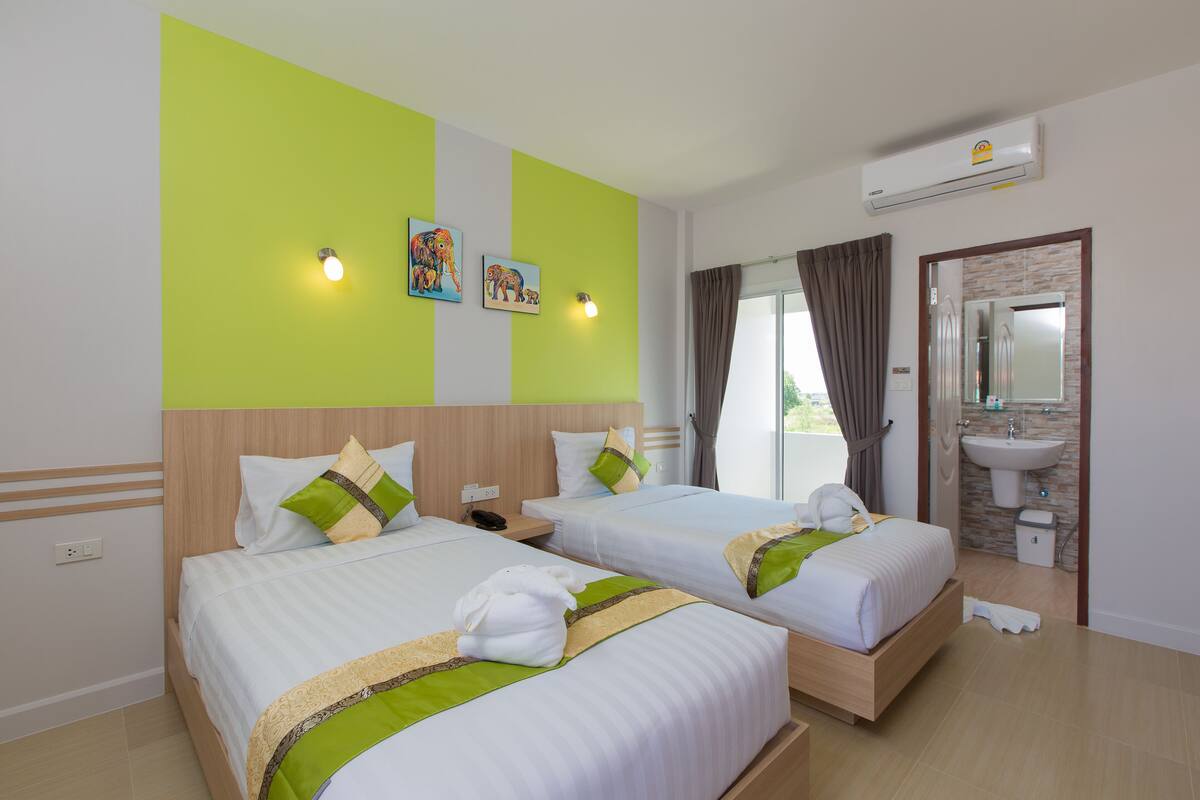 A hotel room with two beds, a bathroom with a sink, and an air conditioning unit.