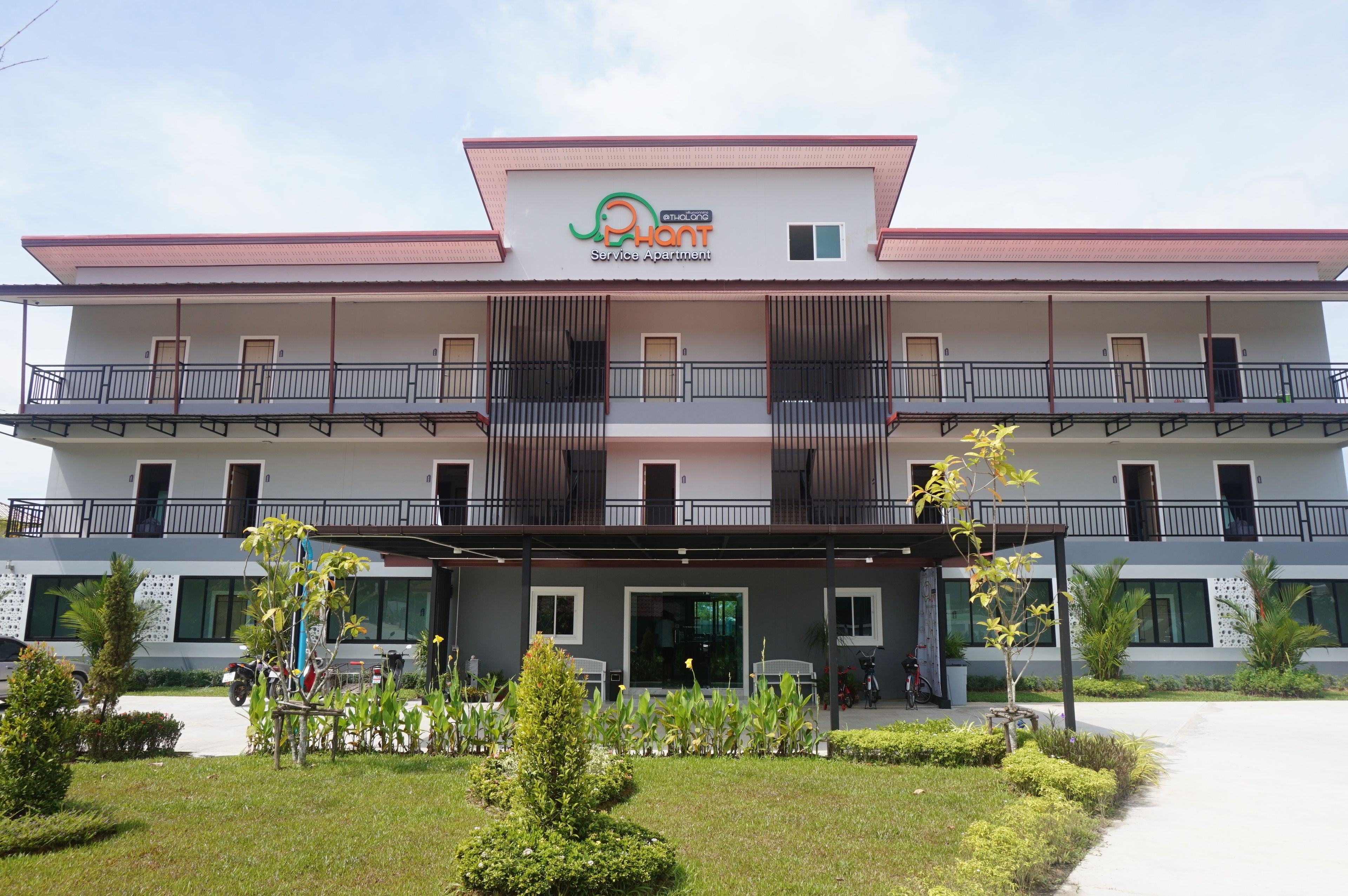 A multi-story building with balconies, a covered entrance, and a garden area.