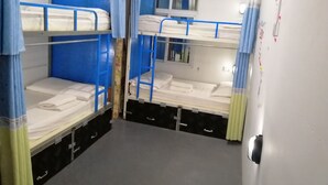 A dormitory room with bunk beds, a small window, and a door with a handle.