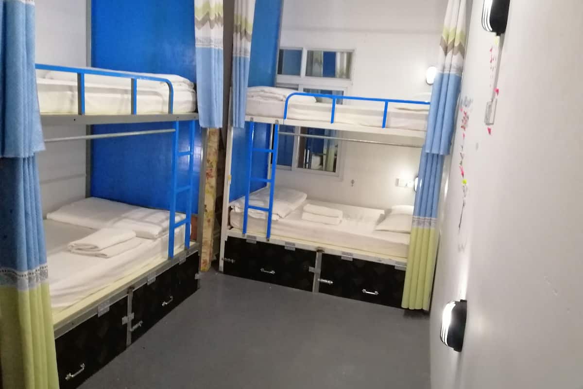 A dormitory room with bunk beds, a small window, and a door with a handle.