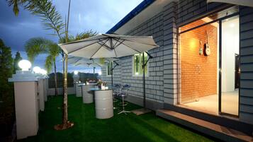 An outdoor patio area with artificial grass, a white umbrella, and several chairs.