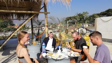 A group of people dining outdoors at a table with a thatched roof overhead.