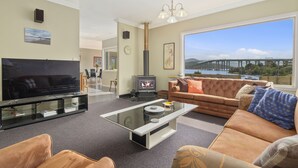 A modern living room with a flat-screen TV, a glass coffee table, a sofa, and a fireplace. - Manfield City Waterfront View Cottage (Rosny)