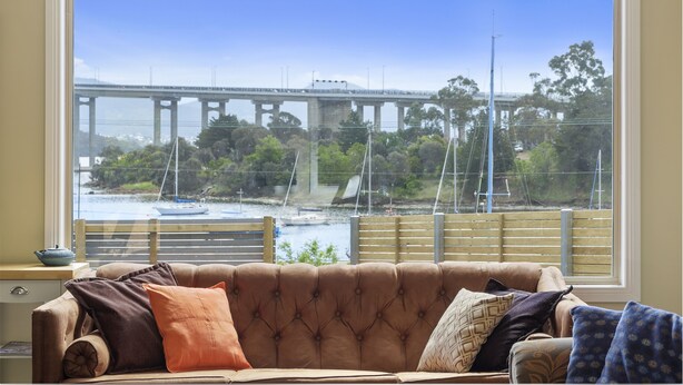 A living room with a large window overlooking a bridge and water. - Manfield City Waterfront View Cottage (Rosny)