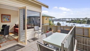A balcony with a table and chairs, a sliding glass door, and a view of a bridge and boats. - Manfield City Waterfront View Cottage (Rosny)