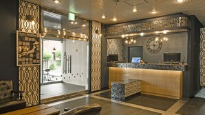 A hotel reception area with a modern design, featuring a reception desk, seating area, and a large window providing a view of the outside. - Hotel AreaOne Tokai (Tokai-mura)