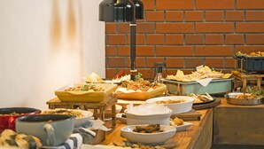 A buffet table with various dishes and a brick wall in the background. - Hotel AreaOne Tokai (Tokai-mura)
