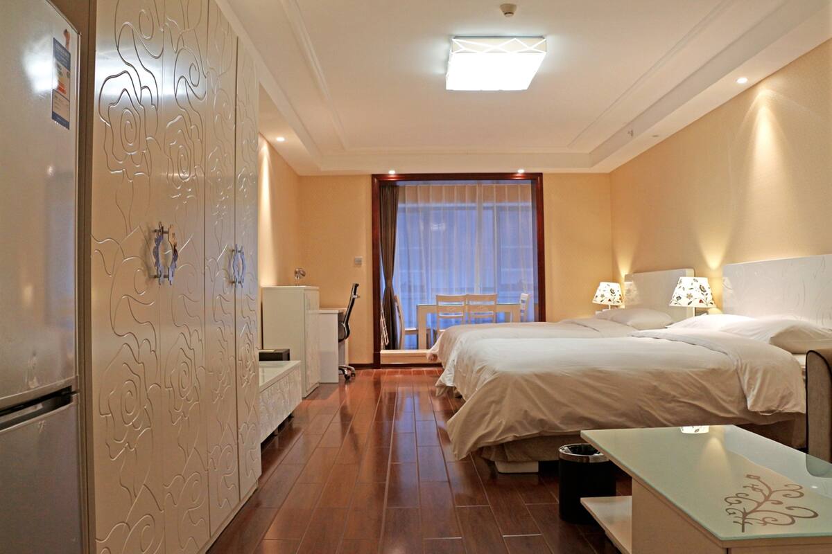 Une chambre d’hôtel comprenant un lit, des tables de chevet, un bureau, une chaise, une armoire et une fenêtre avec des rideaux.