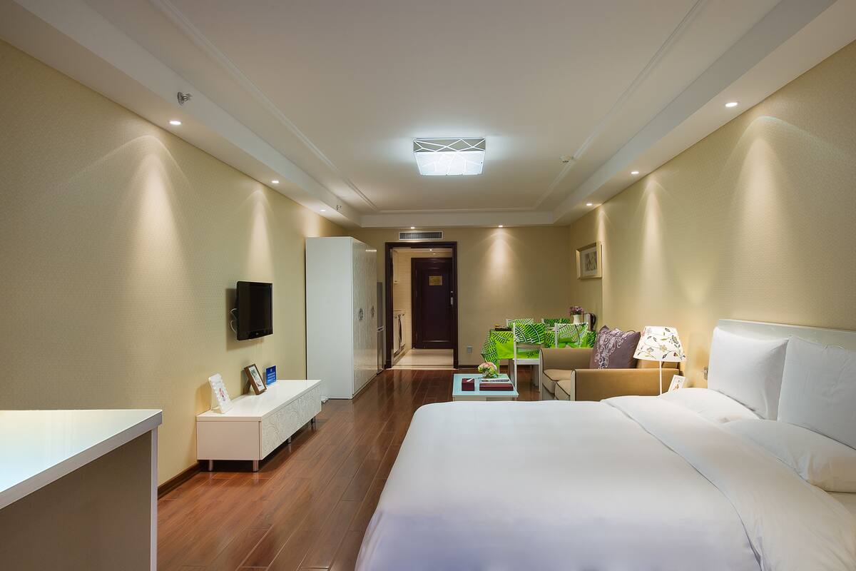 Une chambre d’hôtel avec un lit, une table de chevet, une lampe et un téléviseur fixé au mur.