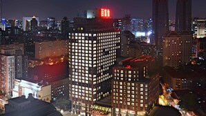 A high-rise building with a prominent red sign at the top, surrounded by other buildings with illuminated windows. - Beijing Baifuyi Apartment Dongzhimen (Beijing)