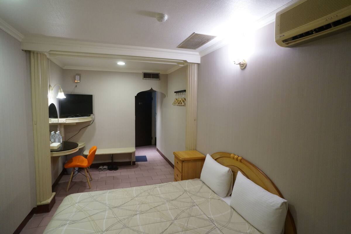 A hotel room with a bed, a desk with a chair, a television, and a wardrobe.