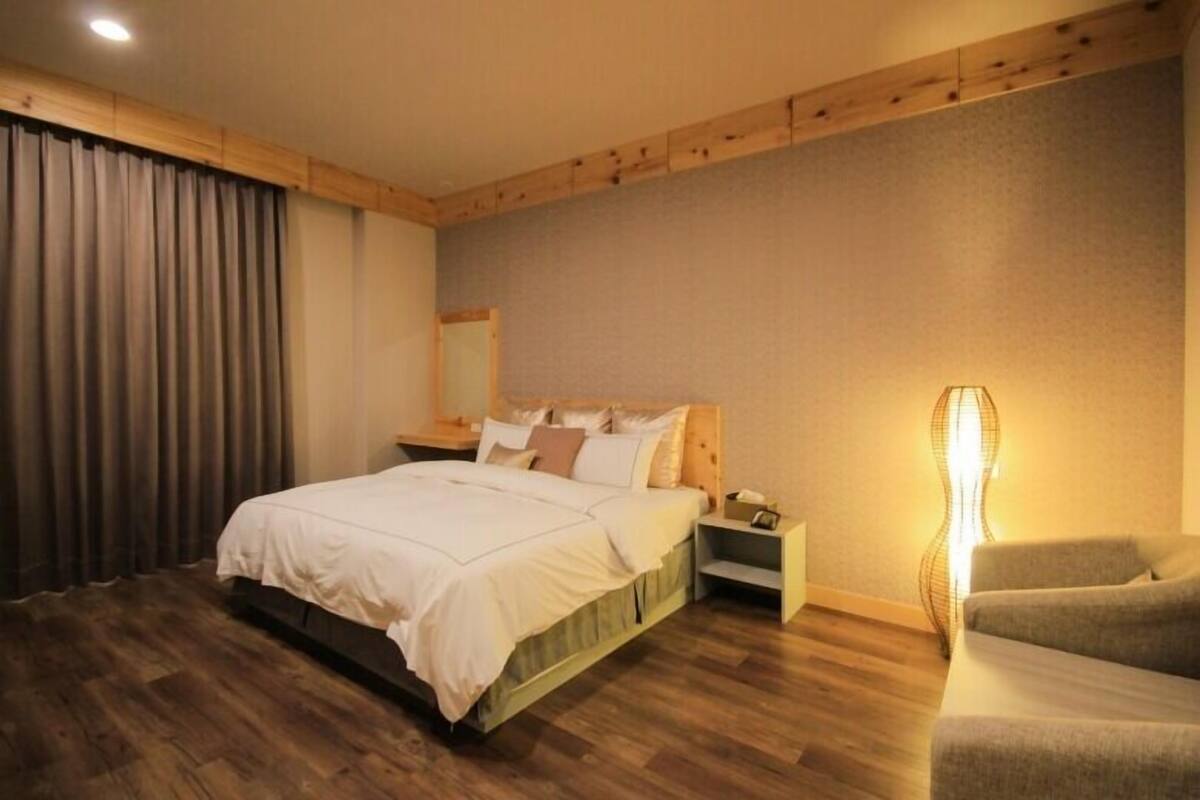 Un dormitorio con cama de cabecera de madera, una mesita de noche, una lámpara y una silla.
