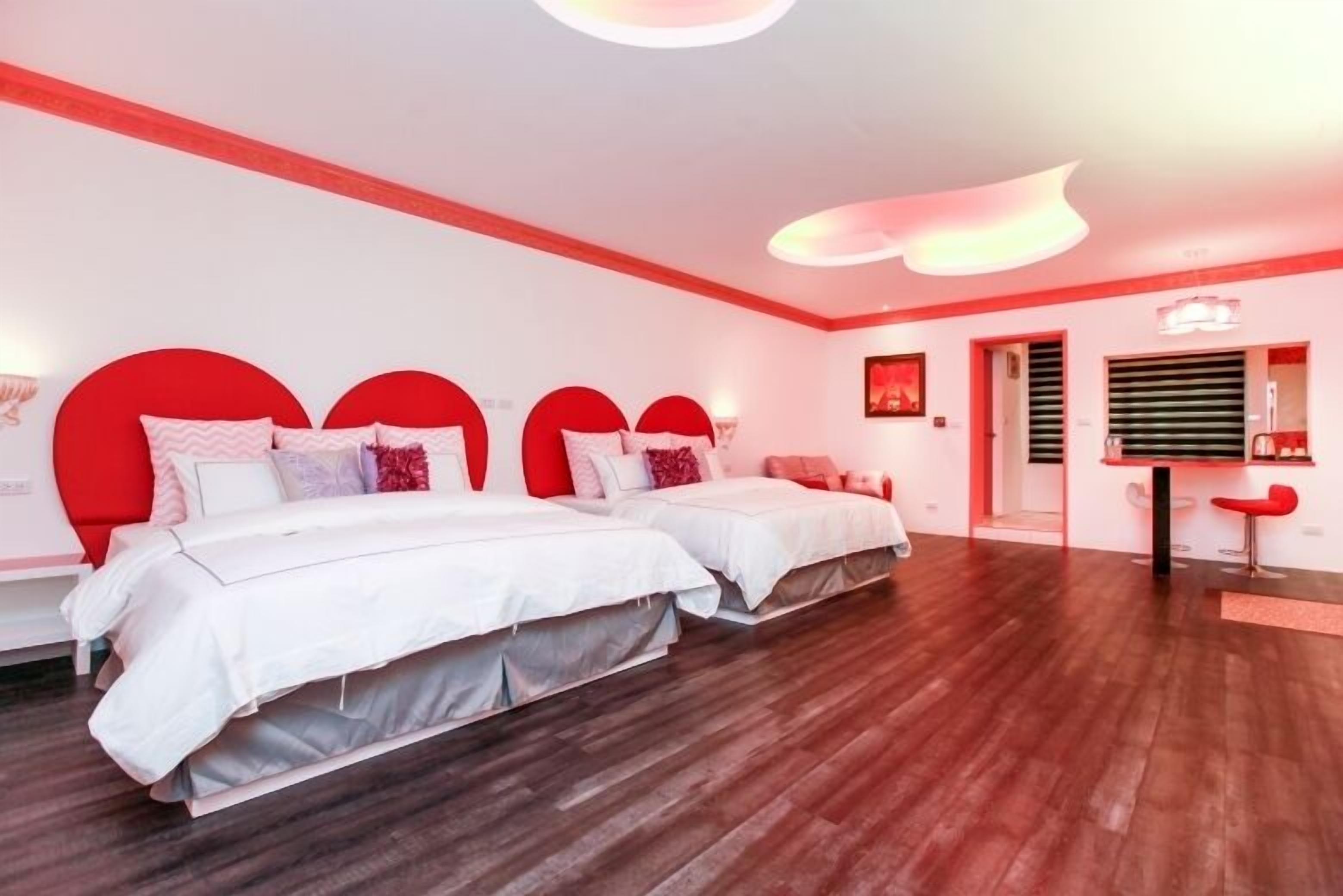 A modern hotel room with two beds, a red accent wall, and a wooden floor.