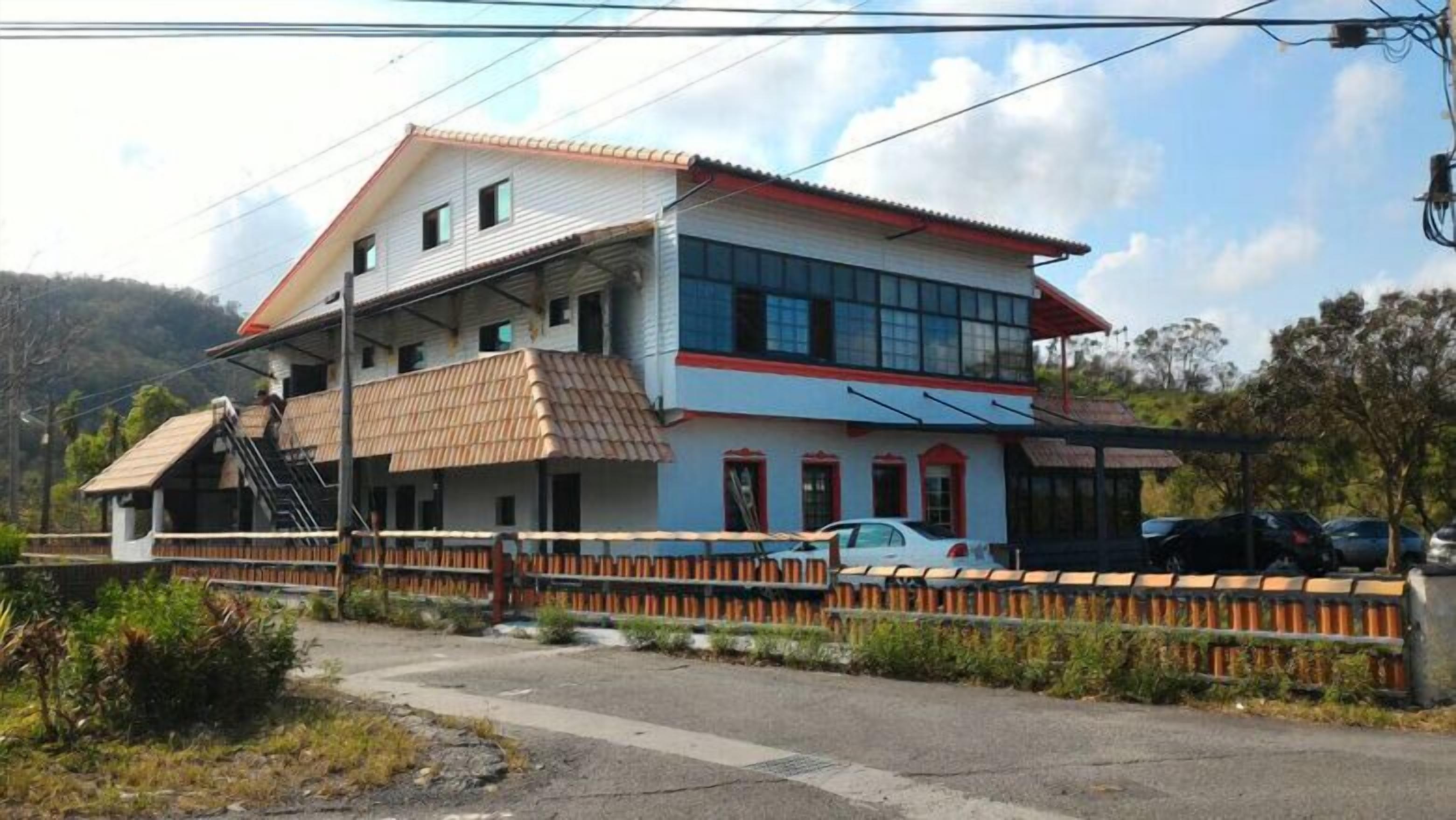 A two-story building with a red roof, a balcony, and a car parked in front.