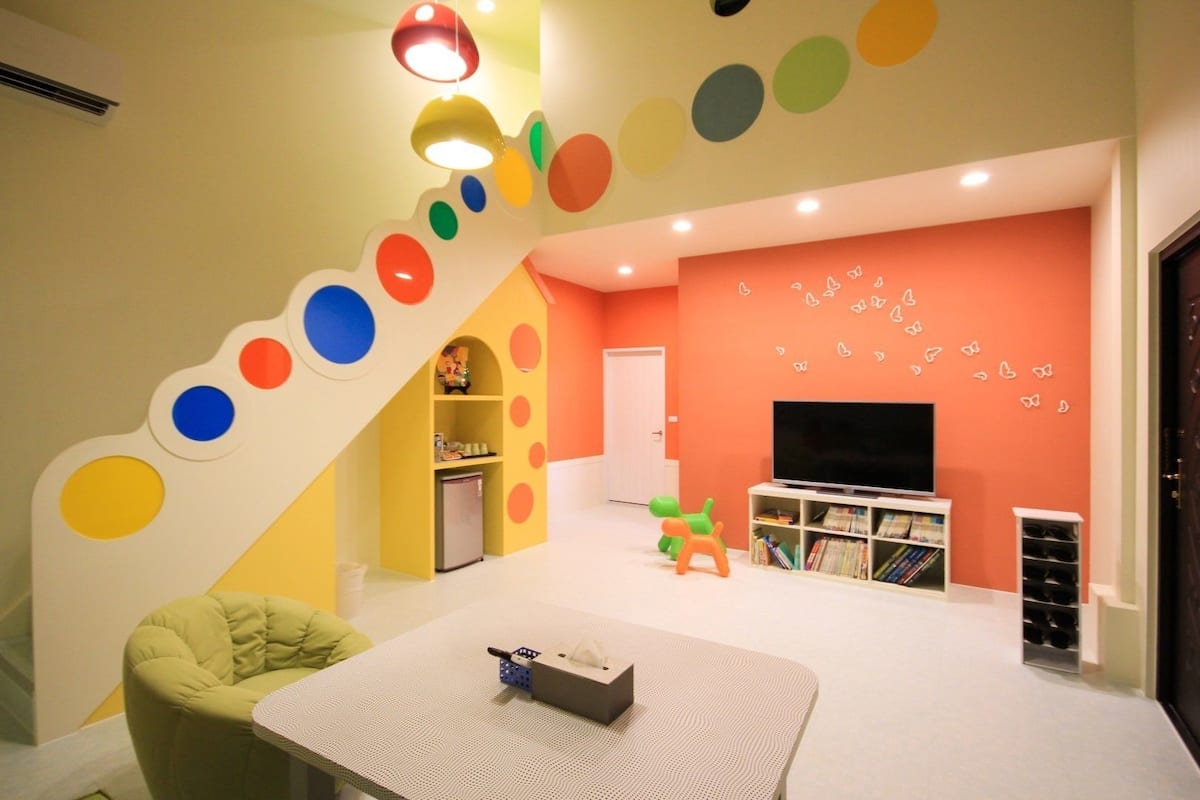 Zona de juegos para niños con una pared colorida, un televisor y una estantería.