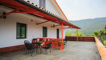 A covered patio with outdoor seating, a brick wall, and a view of a hilly landscape.