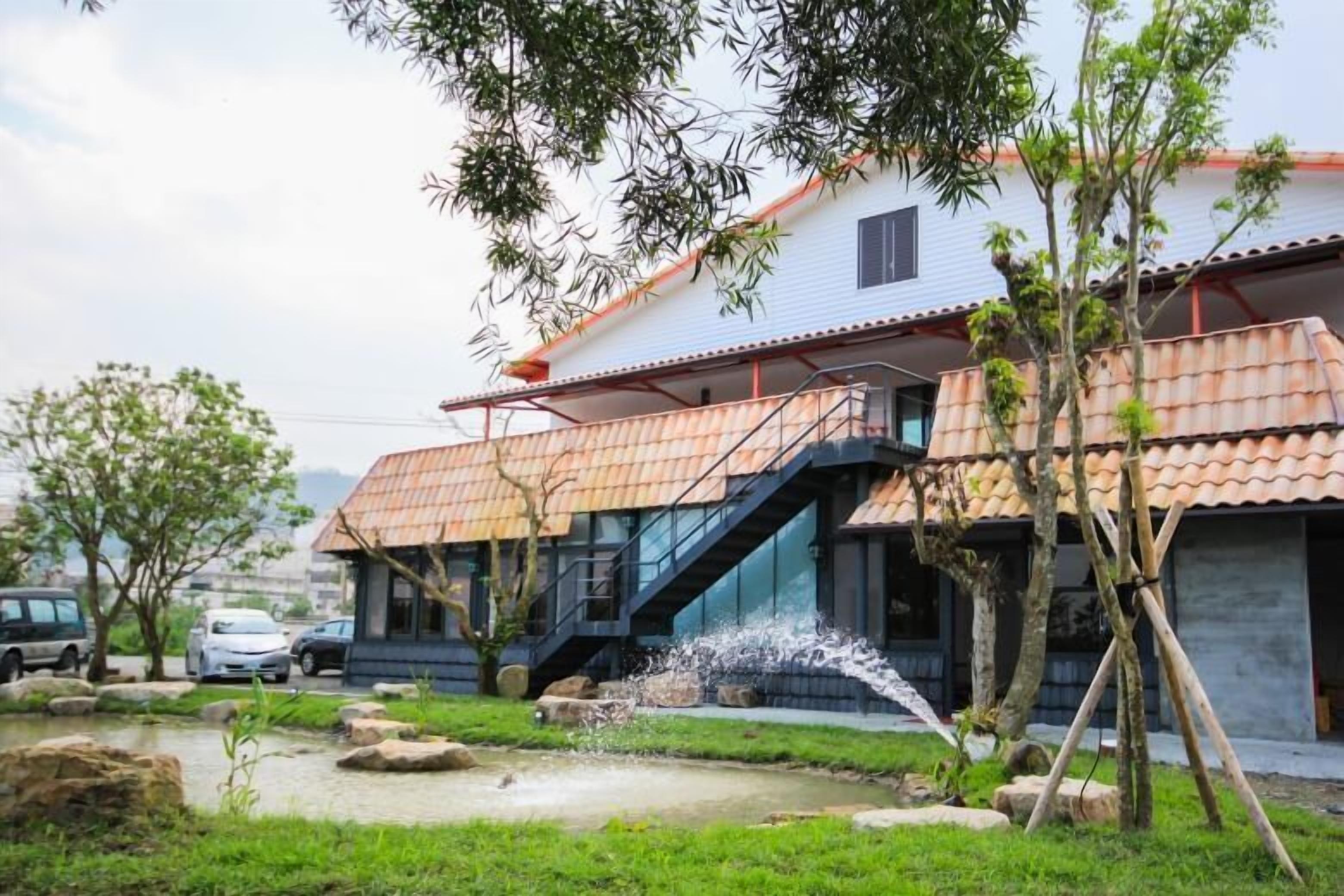 Una casa moderna con techo de tejas, un pequeño jardín con fuente de agua y una escalera que lleva al piso superior.