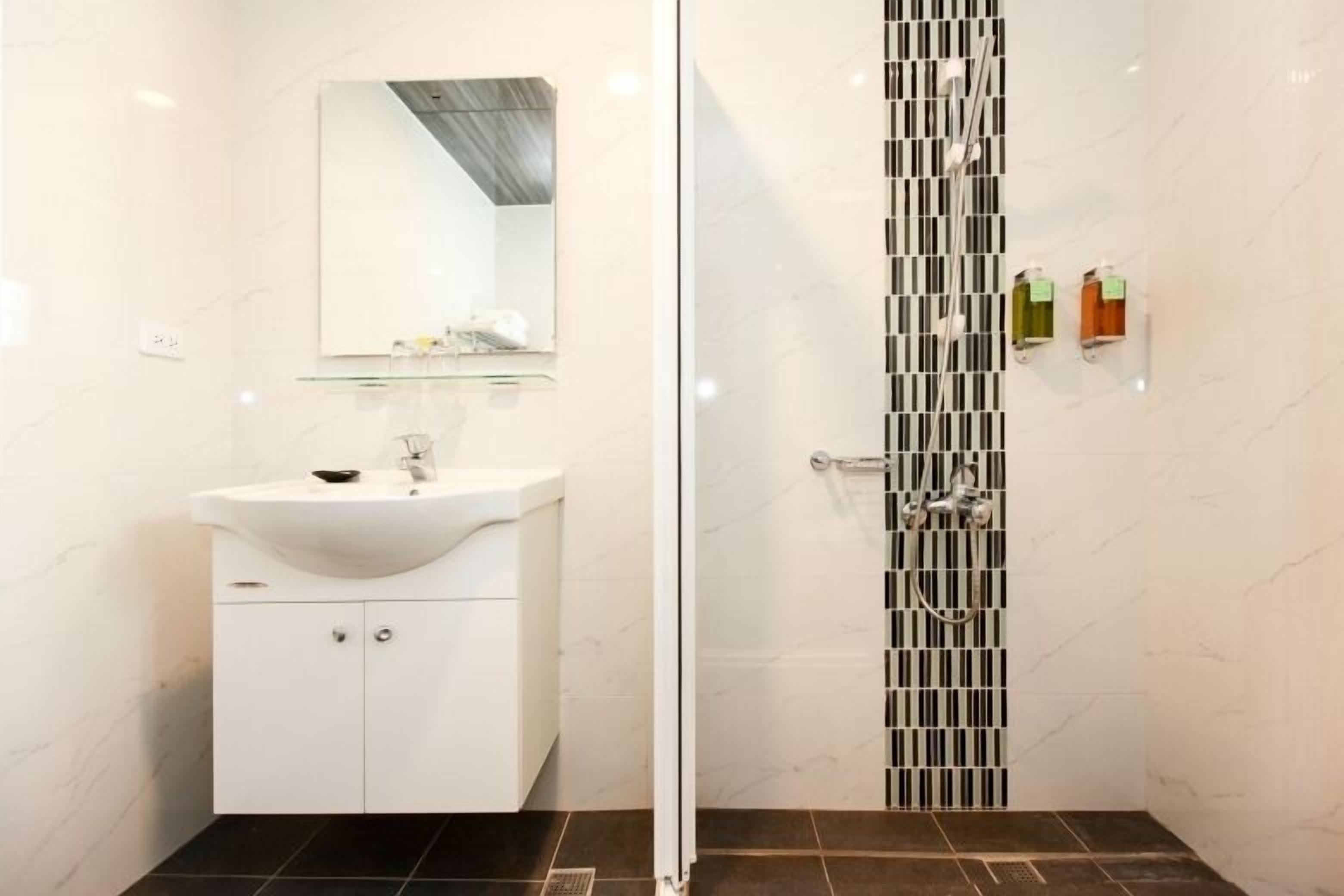 A modern bathroom with a white sink, mirror, and tiled shower enclosure.