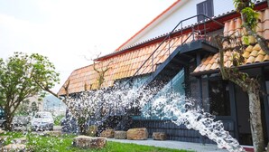 Een gebouw met een schuin dak, een trap die naar een balkon leidt, en een boom op de voorgrond.