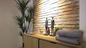 A wooden cabinet with drawers, a potted plant, a small statue, and a folded towel against a brick wall. - Lorong Jambatan Melaka (Malacca City)