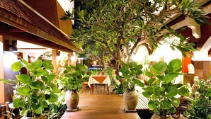 A wooden pathway flanked by large potted plants leading to a table with a white tablecloth. - New Patong Premier Resort (Patong)
