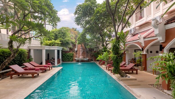 A swimming pool with lounge chairs and a fountain, surrounded by greenery and a building with a tiled roof. - New Patong Premier Resort (Patong)