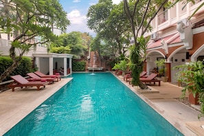 A swimming pool with lounge chairs and a fountain, surrounded by greenery and a building with a tiled roof. - New Patong Premier Resort (Patong)