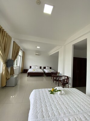 A hotel room with two beds, a desk, a chair, a TV, and an air conditioning unit. - Nha Khach Con Dao (Ho Chi Minh City)