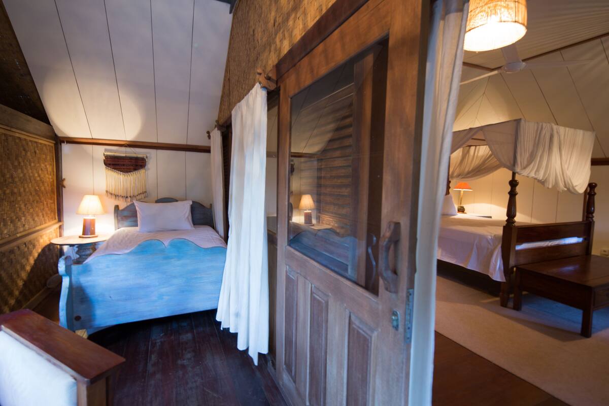 A bedroom with a wooden bed, a nightstand, and a canopy bed in the adjacent room.