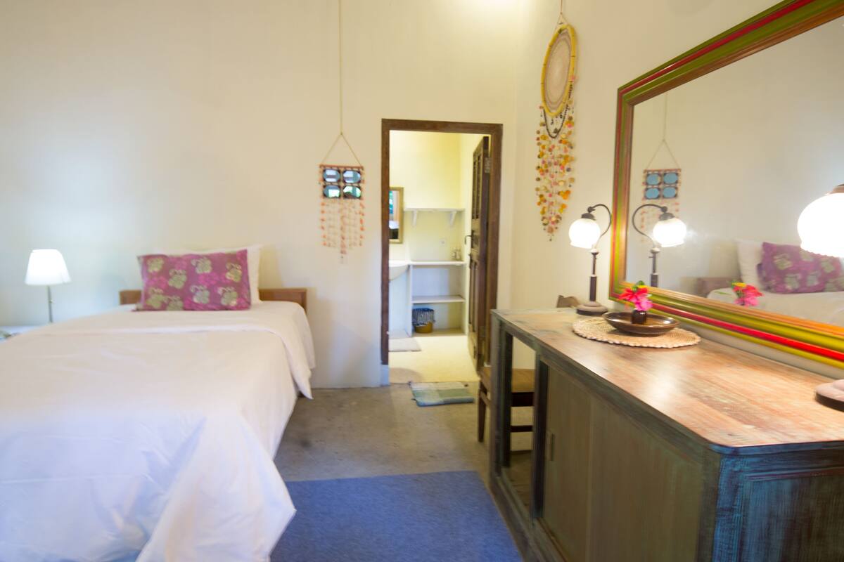 A bedroom with a bed, bedside table, mirror, and a door leading to a bathroom.