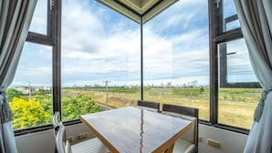 A room with a table and chairs, large windows with curtains, and a view of greenery and buildings. - My Sweetie B&B (Dongshan)