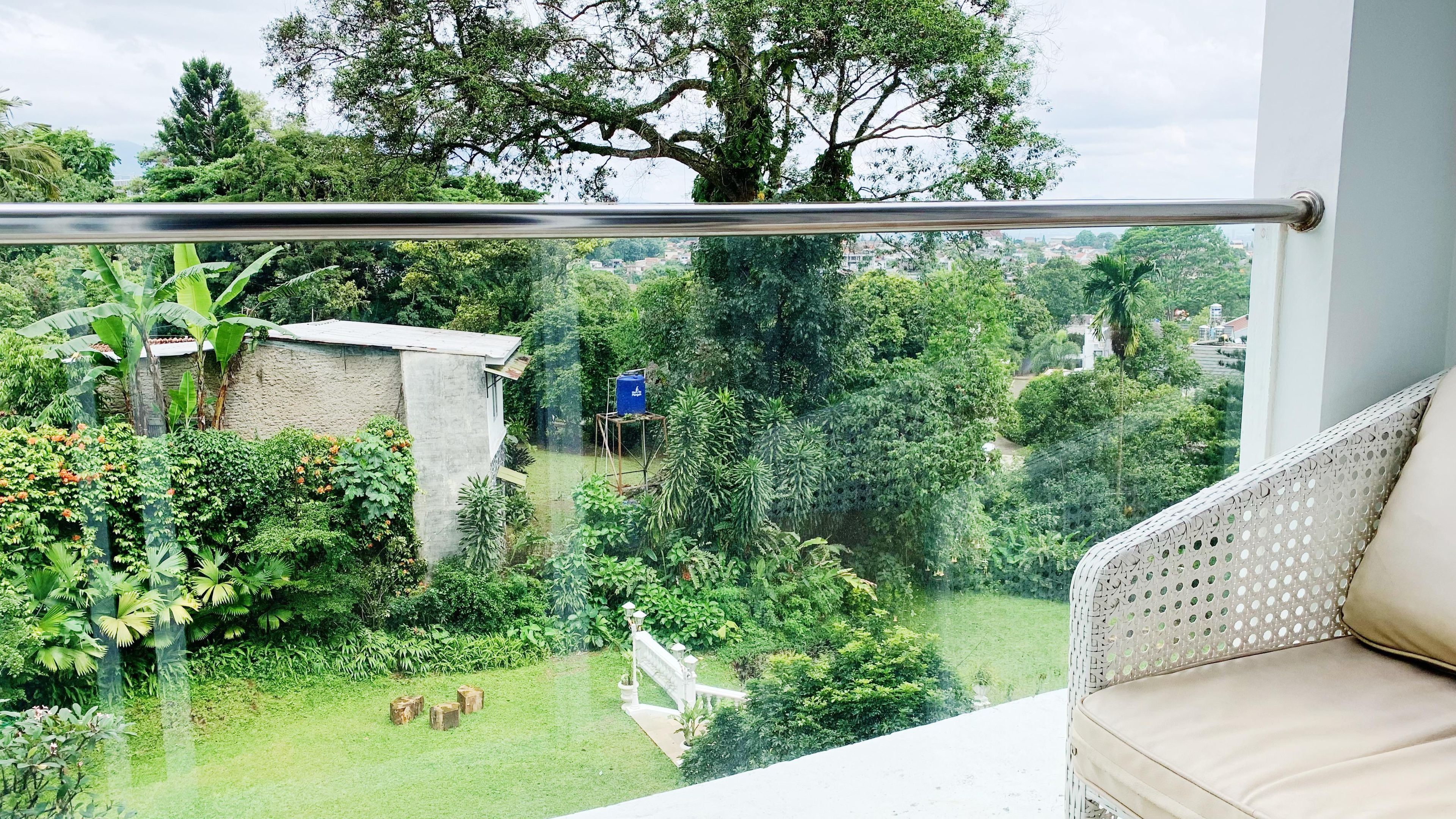 A balcony with a view of a lush garden, a small structure, and a white chair.