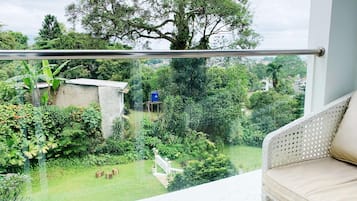 A balcony with a view of a lush garden, a small structure, and a white chair.