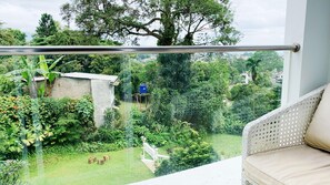Ein Balkon mit Blick auf einen üppigen Garten, eine kleine Struktur und ein weißer Stuhl.