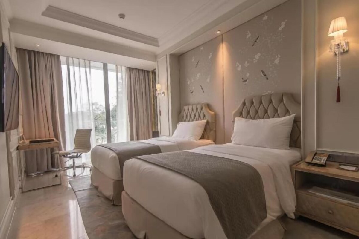 A hotel room with two beds, a desk, a chair, and a large window with curtains.