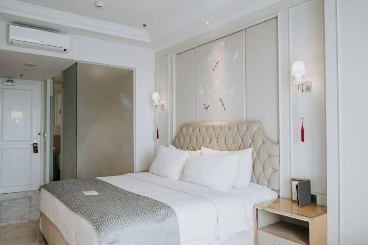 Een hotelkamer met een groot bed, een nachtkastje, een airconditioning en een deur naar een andere kamer.