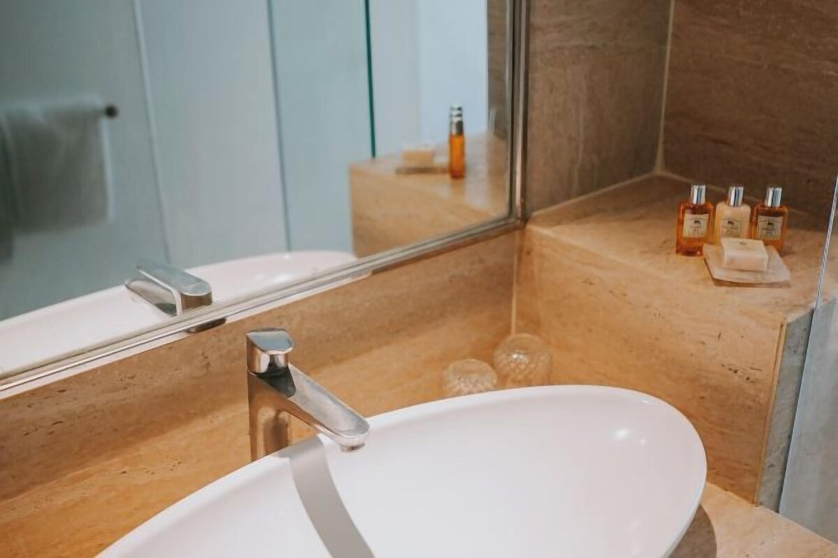 A bathroom with a white sink, a mirror, and a shelf with toiletries.