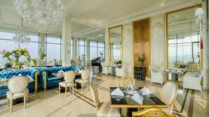 Un hall d’hôtel luxueux, agrémenté d’un imposant lustre, d’un canapé en velours bleu et d’un piano.