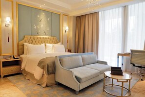 A hotel room with a large bed, a sofa, a small table, and a desk with a chair. - Art Deco Luxury Hotel & Residence (Bandung)