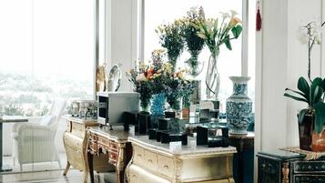 A room with a large window, a white chair, a wooden dresser, and various decorative items including vases and a blue and white ceramic piece.