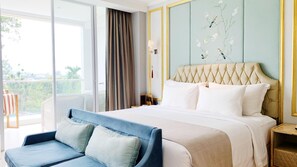 Une chambre d’hôtel avec un grand lit, un canapé bleu, un balcon avec vue et un mur recouvert d’un papier peint à motifs floraux.
