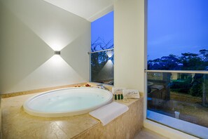 Ein modernes Badezimmer mit einer großen, ovalen Badewanne, einer Duschkabine aus Glas und Blick auf Bäume durch ein großes Fenster.