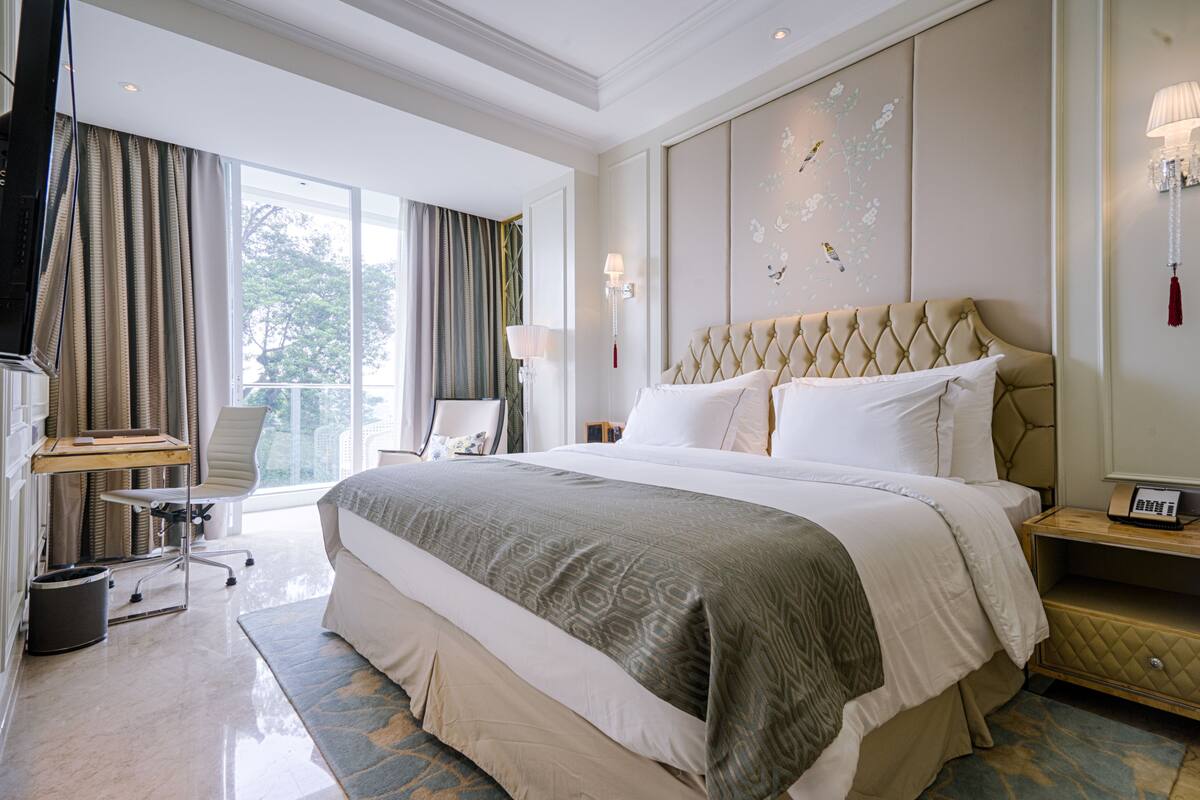 A hotel room with a large bed, a desk, a chair, and a view of the outdoors.