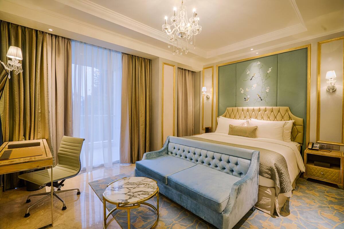 A hotel room with a large bed, a sofa, a desk, and a chandelier.