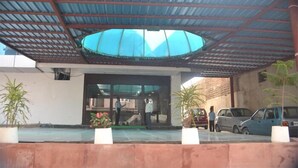 A building entrance with a covered area, potted plants, and parked cars. - Hotel Patliputra Nirvanaa (Patna)