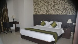 A hotel room with a large bed, a desk with a lamp, and a chair. - Hotel Patliputra Nirvanaa (Patna)